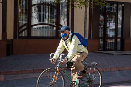 UKRAINE, KYIV - April 25, 2020: Man wearing a medical mask to prevent of bacterial infection Corona virus or Covid 19 epidemic is riding bicycle on the street.のeditorial素材