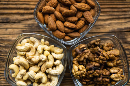Almond, walnut and cashew in a small plates which standing on a wooden vintage table. Nuts is a...