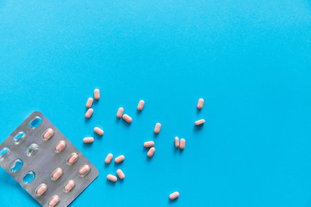 Top view on the pills removed from the pack. Pink pills on blue background. Medicine, medication,...