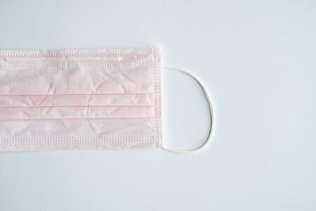 Used pink medical mask on a gray background. Disposable 3-ply medical mask to cover the mouth and nose to prevent coronavirus. Coronavirus quarantine. Antivirus medical mask for protection covid-19.の写真素材