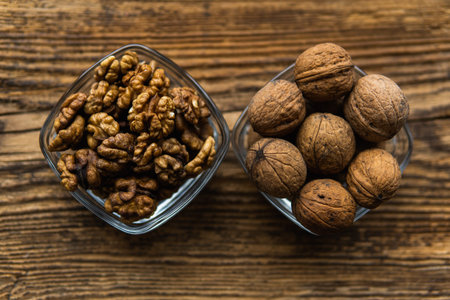 Whole and sheled walnut in a small plates on a vintage wooden table as a background. Walnuts is a...