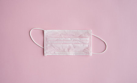 Used pink medical mask on a pink background. Disposable 3-ply medical mask to cover the mouth and...