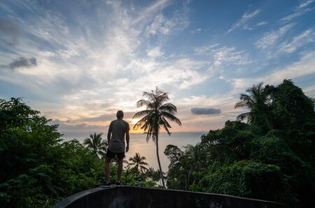 Silhouette of man standing alone on the hill with a coconut palm trees and enjoys sea on a horizon in a sunset. Vacation and travel concept on a island. Beautiful sunsets on a Samui island.の写真素材
