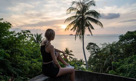 Silhouette of woman sitting alone on the hill with a coconut palm trees and enjoys sea on a horizon in a sunset. Vacation and travel concept on a island. Beautiful sunsets on a Samui island.の写真素材