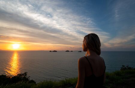 Silhouette of a woman watches sunset over a sea or ocean on a tropical island.の写真素材