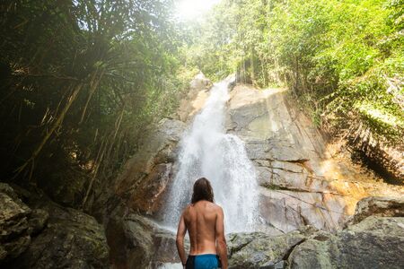 Man with a long hair is enjoy in lagoon of huge tropical waterfall in jungle. Travel conceptの写真素材