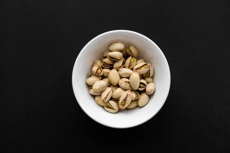 Pistachios in a small plate on a black table. Pistachio is a healthy vegetarian protein nutritious food. Natural nuts snacks.の写真素材