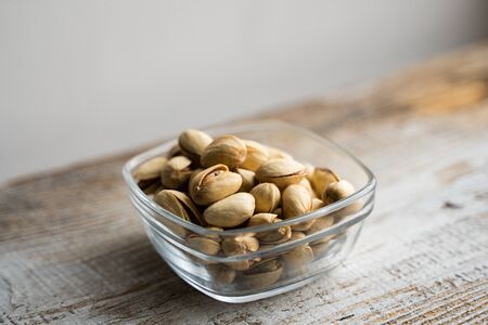 Pistachios in a small plate on a vintage wooden table. Pistachio is a healthy vegetarian protein nutritious food. Natural nuts snacks.の写真素材