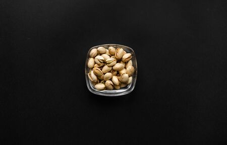 Pistachios in a small plate on a black table. Pistachio is a healthy vegetarian protein nutritious food. Natural nuts snacks.の写真素材