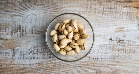 Pistachios in a small plate on a vintage wooden table. Pistachio is a healthy vegetarian protein nutritious food. Natural nuts snacks.の写真素材