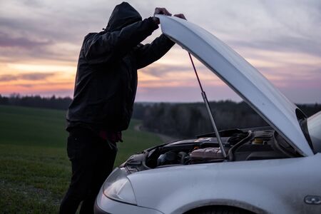 Man standing near car with open hood on sunset. Car breakdown. Confused man stands with open hood with selective soft focus.の写真素材