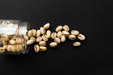 Pistachio scattered on the black table from a jar. Walnut is a healthy vegetarian protein nutritious...