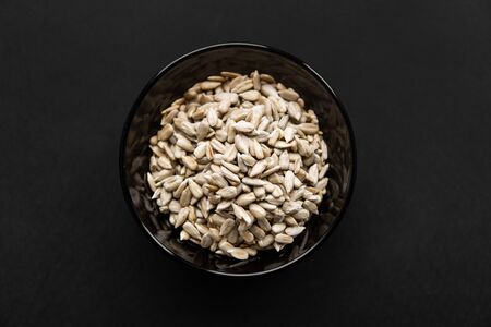 Sunflower seeds in a small plate on the black table. Healthy vegetarian protein nutritious food. Sunflower seed on rustic old wood.の写真素材