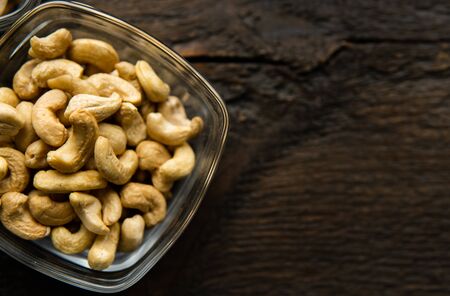 Cashew nuts in a small plate on a vintage wooden table as a background. Cashew nut is a healthy vegetarian protein nutritious food.の写真素材