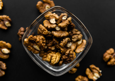 Walnut in a small plate with scattered shelled nuts which standing on a black surface. Walnuts is a...