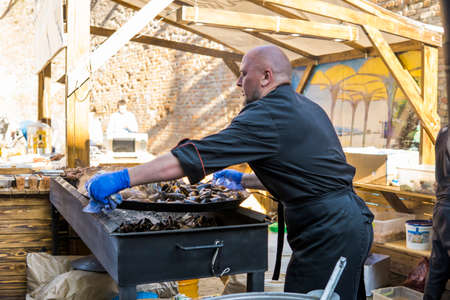 UKRAINE, LUTSK - June 5, 2019: Man is cooking a fresh mussels in shells in large metallic grill pan on a food fest.のeditorial素材