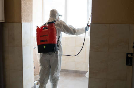 UKRAINE, KYIV - May 20, 2020: Man in a white protective suit and mask is sanitizing interior surfaces inside buildings while the coronavirus epidemic for infection prevention and control of epidemicのeditorial素材