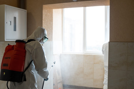 UKRAINE, KYIV - May 20, 2020: Man in a white protective suit and mask is sanitizing interior surfaces inside buildings while the coronavirus epidemic for infection prevention and control of epidemic.のeditorial素材