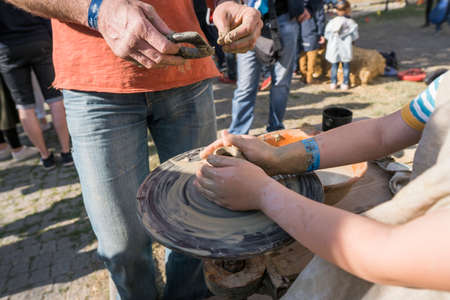 UKRAINE, LUTSK - June 5, 2019: The hands of an adult man teaching pottery the child how to make a jug from a piece of clay on a Potters wheel on a food fest.のeditorial素材