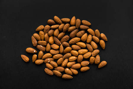 Almonds scattered on a black table. Almond is a healthy vegetarian protein nutritious food. Natural nuts snacks.の写真素材