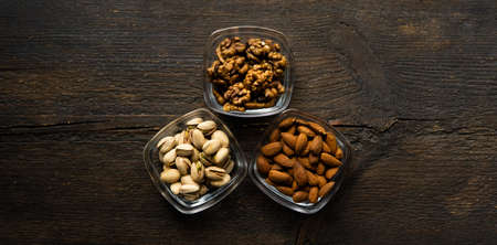 Almond, pistachio and walnut in a small plates which standing on a vintage wooden table. Nuts is a healthy vegetarian protein and nutritious food.の写真素材