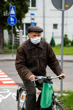 UKRAINE, KYIV - April 25, 2020: Man wearing a medical mask to prevent of bacterial infection Corona virus or Covid 19 epidemic is riding bicycle on the street.のeditorial素材
