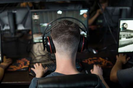 POLAND, WARSAW - June 10, 2020: Back view of young gamer in headphone playing video game at computer club.のeditorial素材