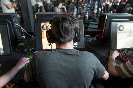 POLAND, WARSAW - June 10, 2020: Back view of young gamer in headphone playing video game at computer clubのeditorial素材