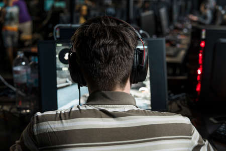 POLAND, WARSAW - June 10, 2020: Back view of young gamer in headphone playing video game at computer clubのeditorial素材