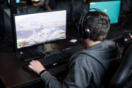POLAND, WARSAW - June 10, 2020: Back view of young gamer in headphone playing video game at computer clubのeditorial素材