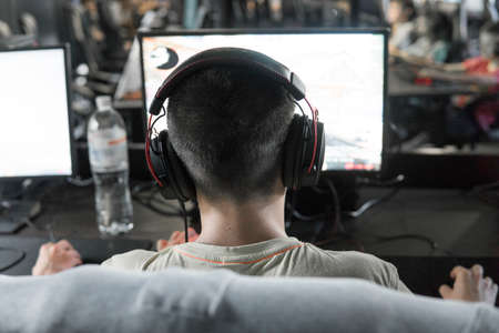 POLAND, WARSAW - June 10, 2020: Back view of young gamer in headphone playing video game at computer clubのeditorial素材