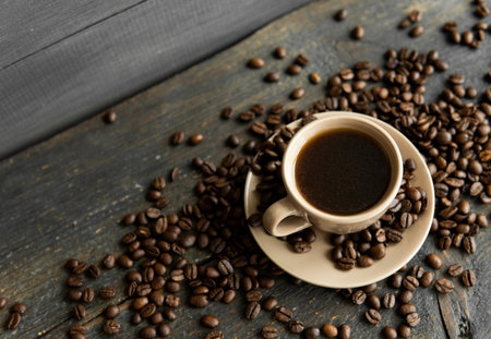 Coffee cup with roasted coffee beans on wooden table background. Mug of black coffe with scattered...