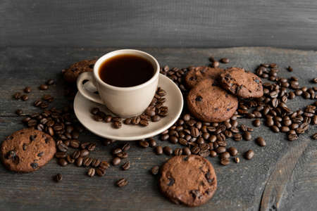 Coffee cup with cookies on wooden table background. Mug of black coffee with scattered coffee beans and cookies on a wooden table. Fresh coffee beans.の写真素材