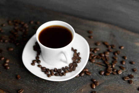 Coffee cup with roasted coffee beans on wooden table background. Mug of black coffe with scattered...