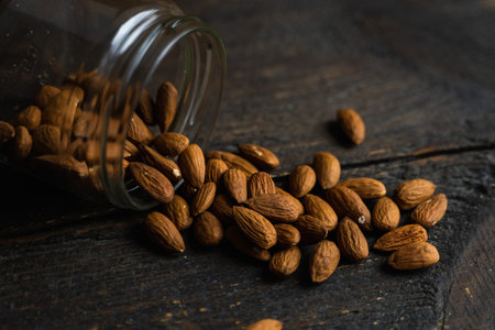 Almonds scattered on the wooden vintage table from a jar. Almond is a healthy vegetarian protein...
