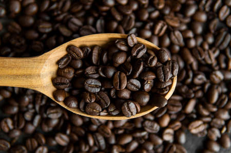 Fresh roasted arabica coffee beans in a wooden spoon and scattered coffee beans on a wooden table.の写真素材