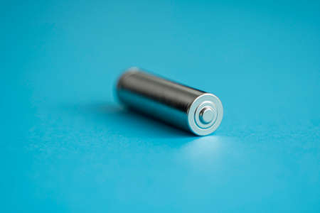 A single rechargeable battery on blue background. Silver alkaline AA battery for different device. Energy.の写真素材
