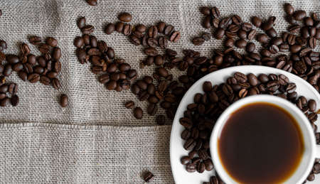 Coffee cup with roasted coffee beans on linen background. Mug of black coffe with scattered coffee beans. Fresh coffee beans.の写真素材