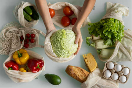 Woman hand holding Reusable eco textile grocery bag with vegetables and takes cabage out. Zero waste and plastic free concept. Girl is holding mesh cotton shopper with vegetables.の素材 [FY310155133620]