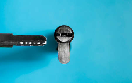 A door lock cylinder core with key on the blue background. The cylinder of the lock with key. Installing a new lock on the door. Spare parts for the door.の写真素材