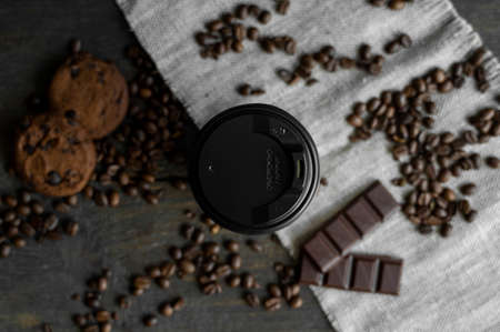 Paper cup of coffee with roasted coffee beans on wooden table. Mug of black coffee with a cookies and chocolate on a table.の写真素材