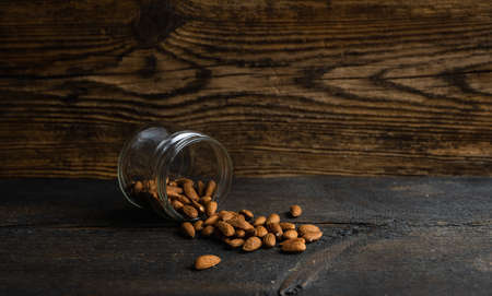 Almonds scattered on the wooden vintage table from a jar. Almond is a healthy vegetarian protein nutritious food. Almonds on rustic old wood.の写真素材