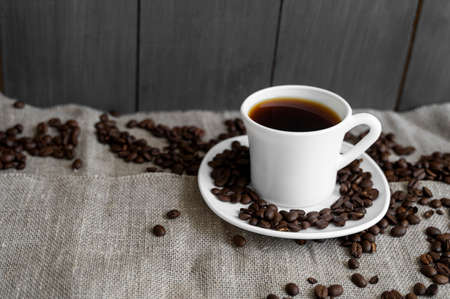 Coffee cup with roasted coffee beans on linen background. Mug of black coffe with scattered coffee beans. Fresh coffee beans.の写真素材