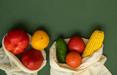 Vegetables in eco bag on green surface with a copy space. Pepper, tomato, corn, cucumber, broccoli,...