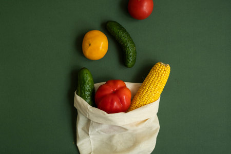 Vegetables in eco bag on green surface. Pepper, tomato, corn, cucumber, broccoli, cauliflower in...