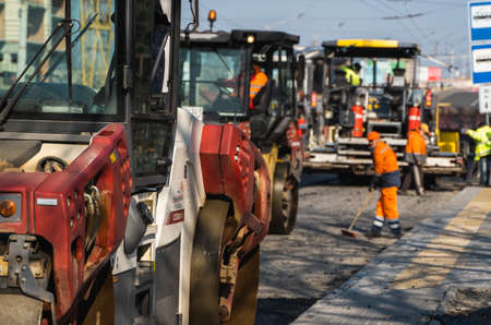 KYIV, UKRAINE - September 10, 2020: Heavy asphalt road roller with heavy vibration roller compactor that press new hot asphalt and asphalt paver machine on a road construction site on a street.のeditorial素材
