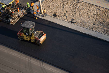KYIV, UKRAINE - September 10, 2020: Heavy asphalt road roller with heavy vibration roller compactor that press new hot asphalt and asphalt paver machine on a road construction site on a street.のeditorial素材