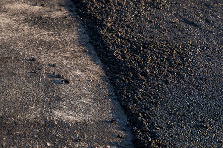 Freshly laid black bitumen asphalt with a high edge to the gravel showing the structure. Laying a...