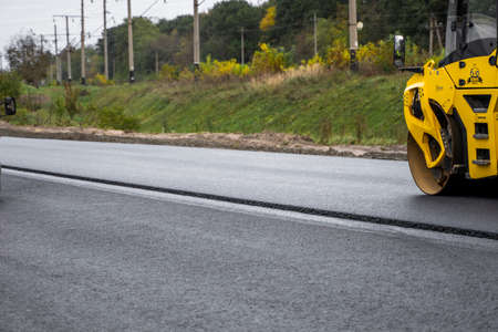 KYIV, UKRAINE - September 25, 2020: Heavy yellow asphalt road roller with heavy vibration roller compactor that press new hot asphalt on the roadway on a road construction site on a street.のeditorial素材
