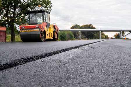 Asphalt road roller with heavy vibration roller compactor press new hot asphalt on the roadway on a road construction site. Heavy Vibration roller at asphalt pavement working. Repairing.の写真素材